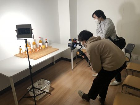 ディレクターの清水さんと、フォトグラファーの山本さんが、ジュースなどの加工品を並べて動画撮影を行っている風景。